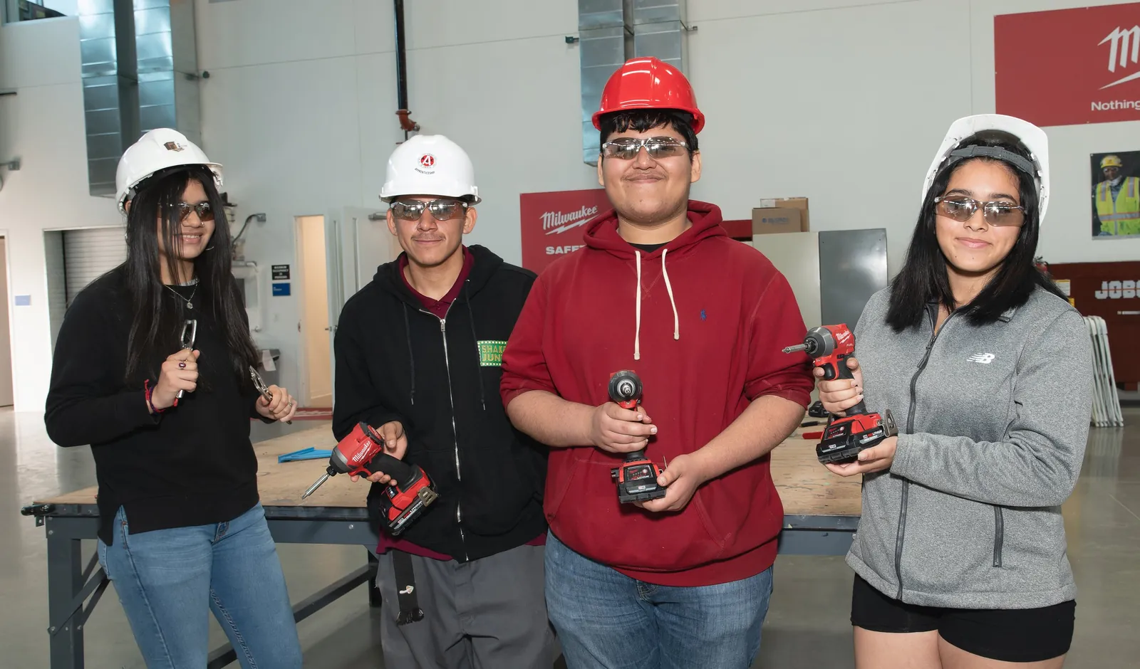 Students holding power tools and smiling during a hands-on trades workshop