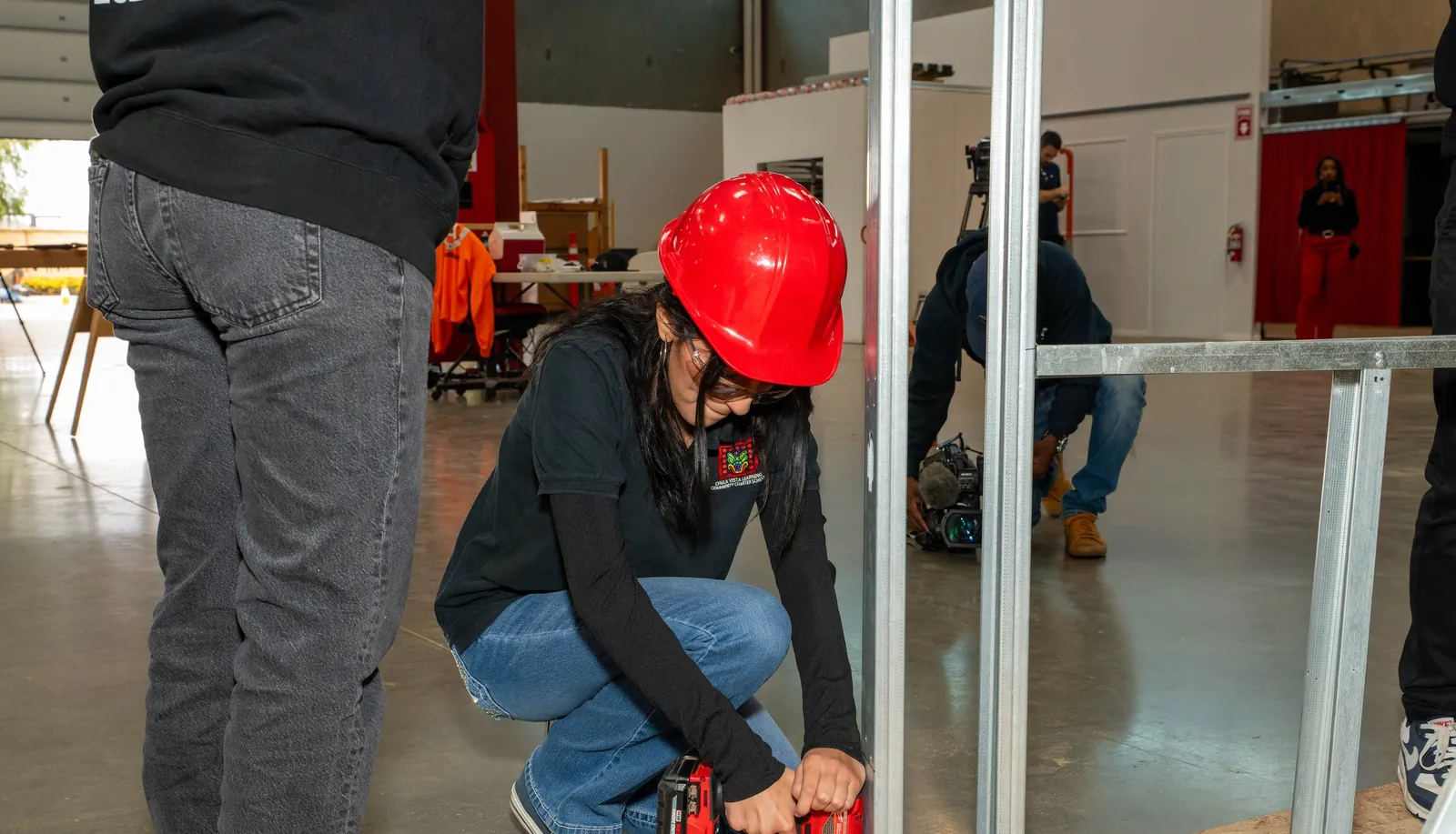 A student in a hard hat using a cordless drill on a metal stud frame